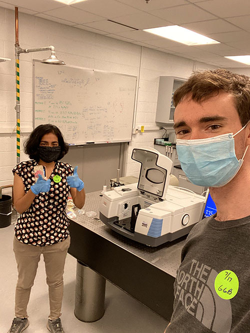 Rohini Bala Chandran (left) and Mike Mayer (right) give thumbs up showing their social distance and PPE in their lab.