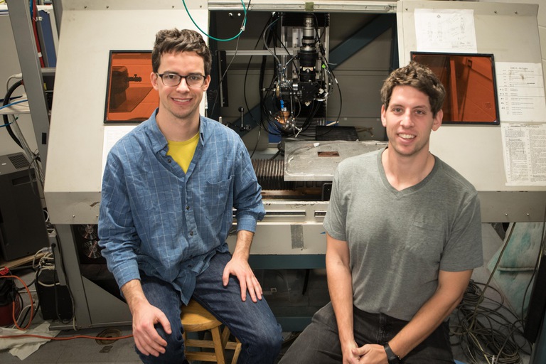 MSE PhD Candidates, Ethan Sprague and Max Powers pose in front of the Laser Direct Metal Disposition in the Mazumder lab.