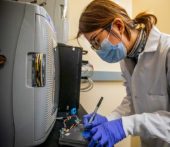 Female research leans over testing equipment verifying the charge of lithium metal
