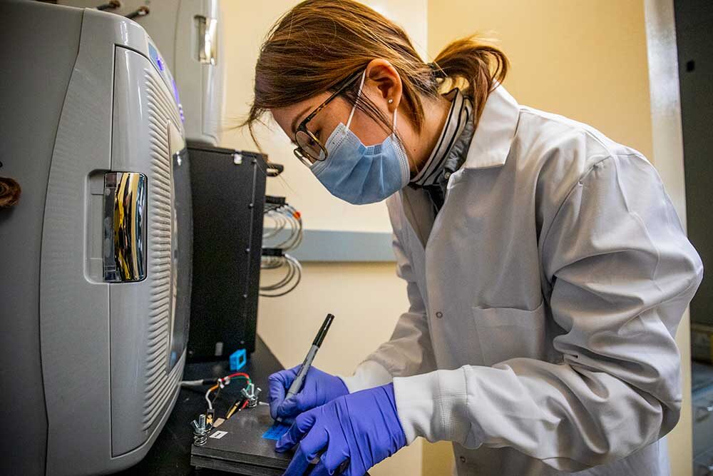 Female research leans over testing equipment verifying the charge of lithium metal