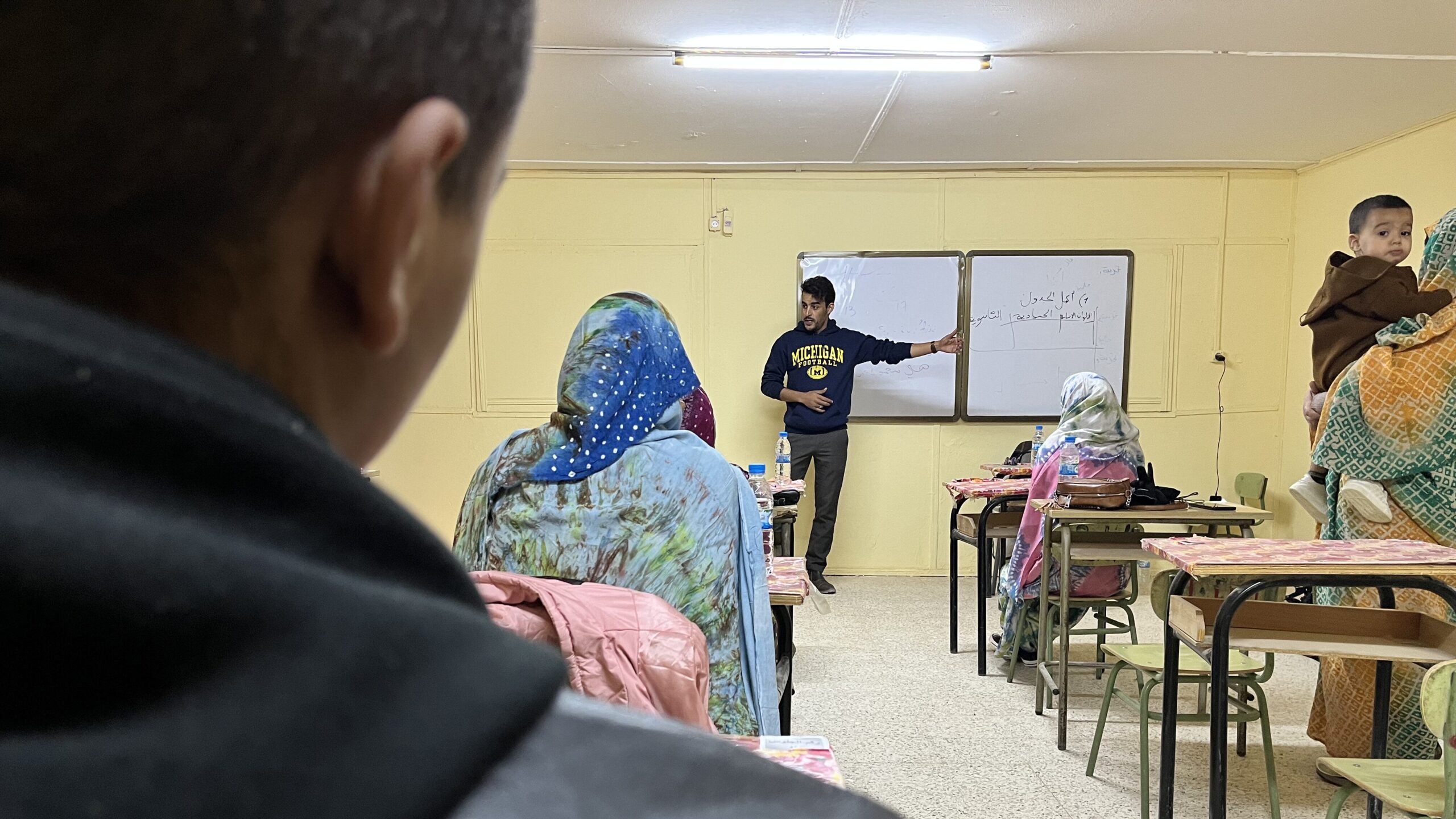 Bachir standing at the front of a classroom, presenting on UWC scholarship opportunities. Students and parents sit facing Bachir.