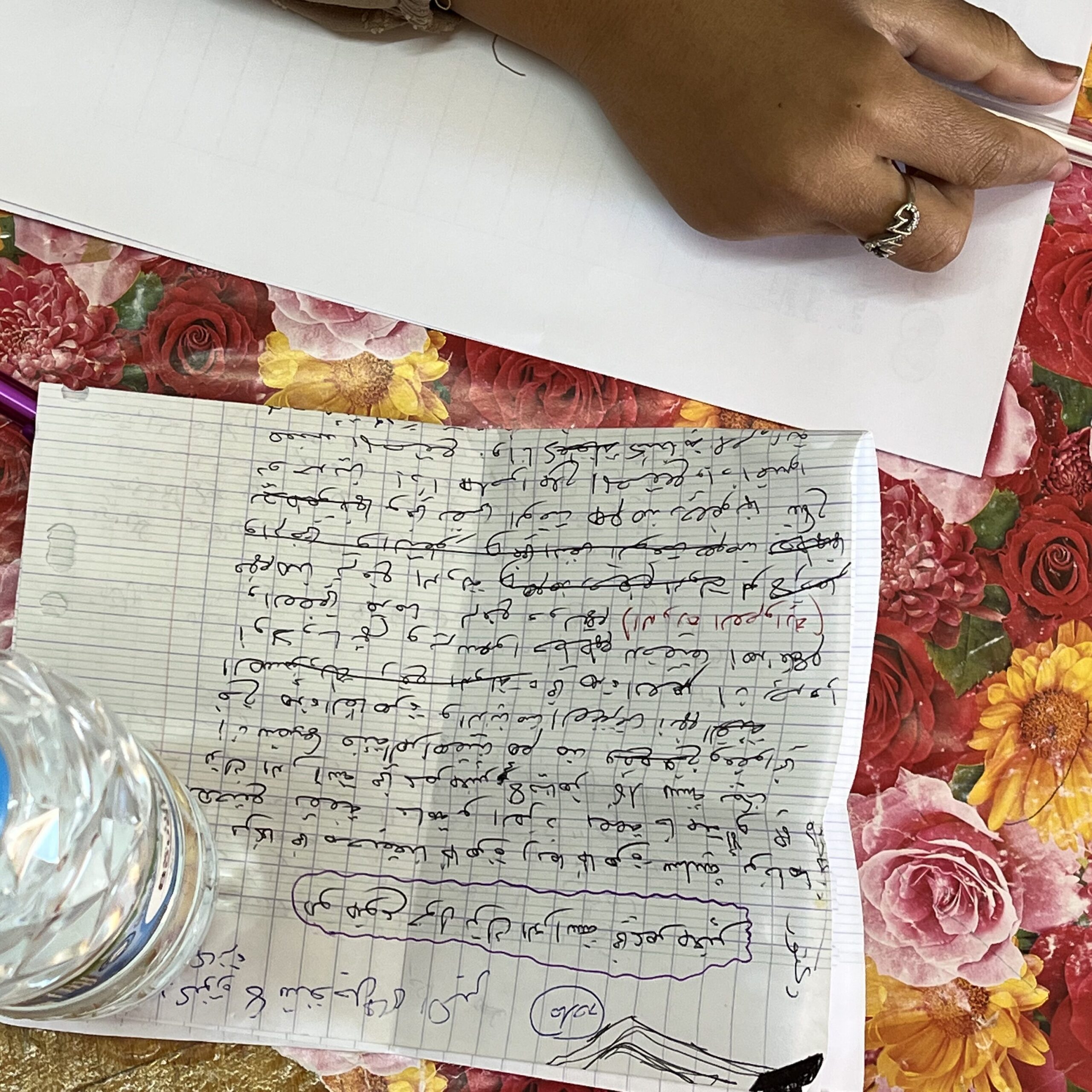 A piece of paper on which is written lines of Arabic text. A woman's hand holding a pen.
