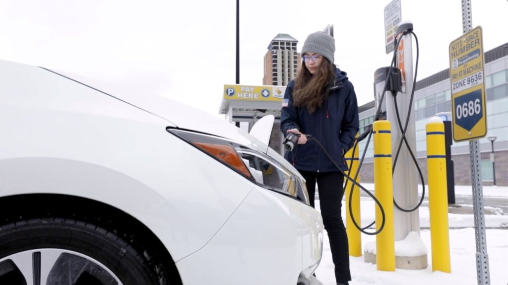 Student plugs in an electric vehicle in snowy weather on the University of Michigan North Campus.