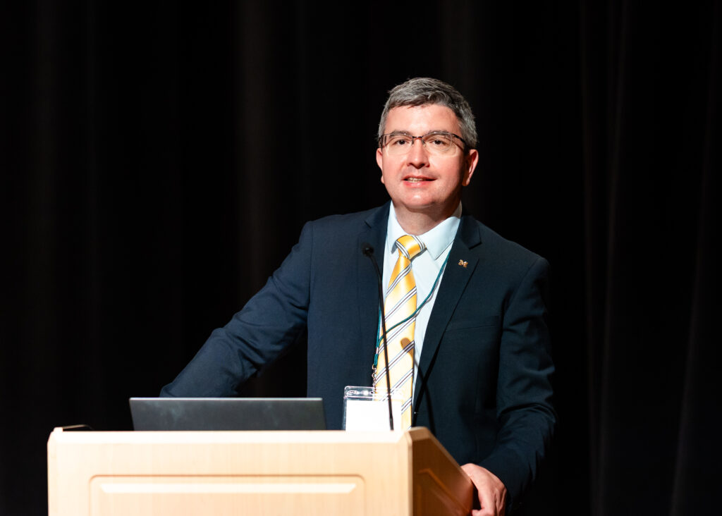 Prof. Bogdan Epureanu, Director of the Automotive Research Center, smiles while standing in front of a podium while speaking